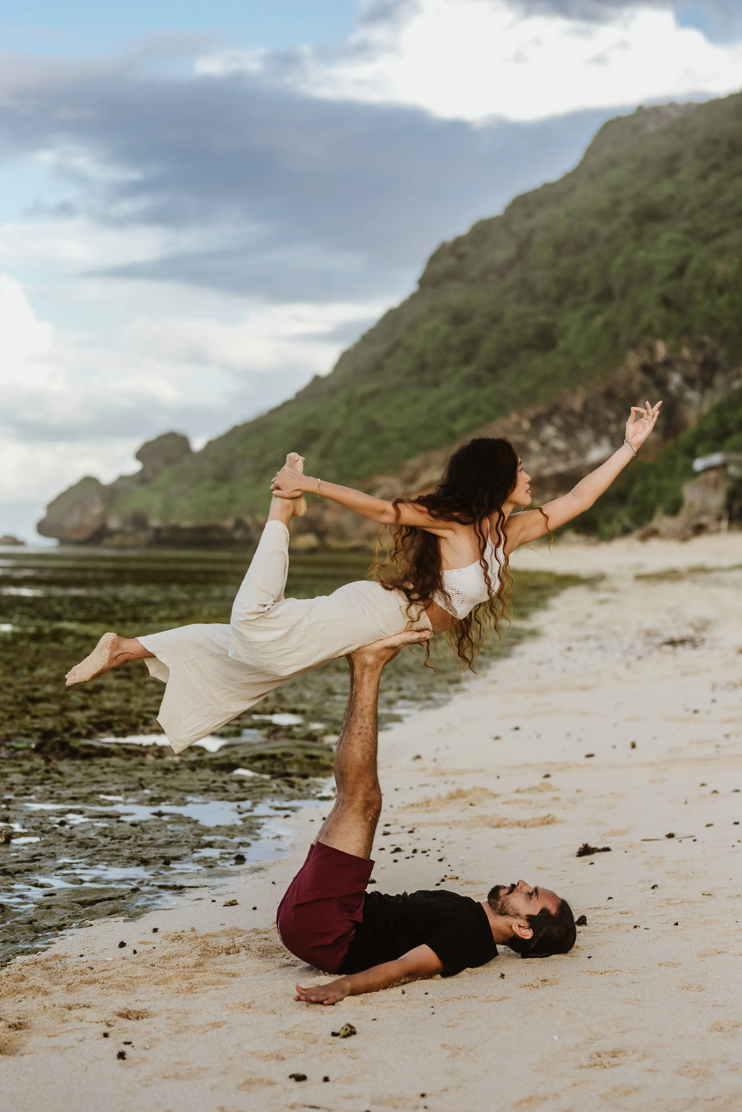 An acroyoga pair balancing in a lifted pose on a beach.