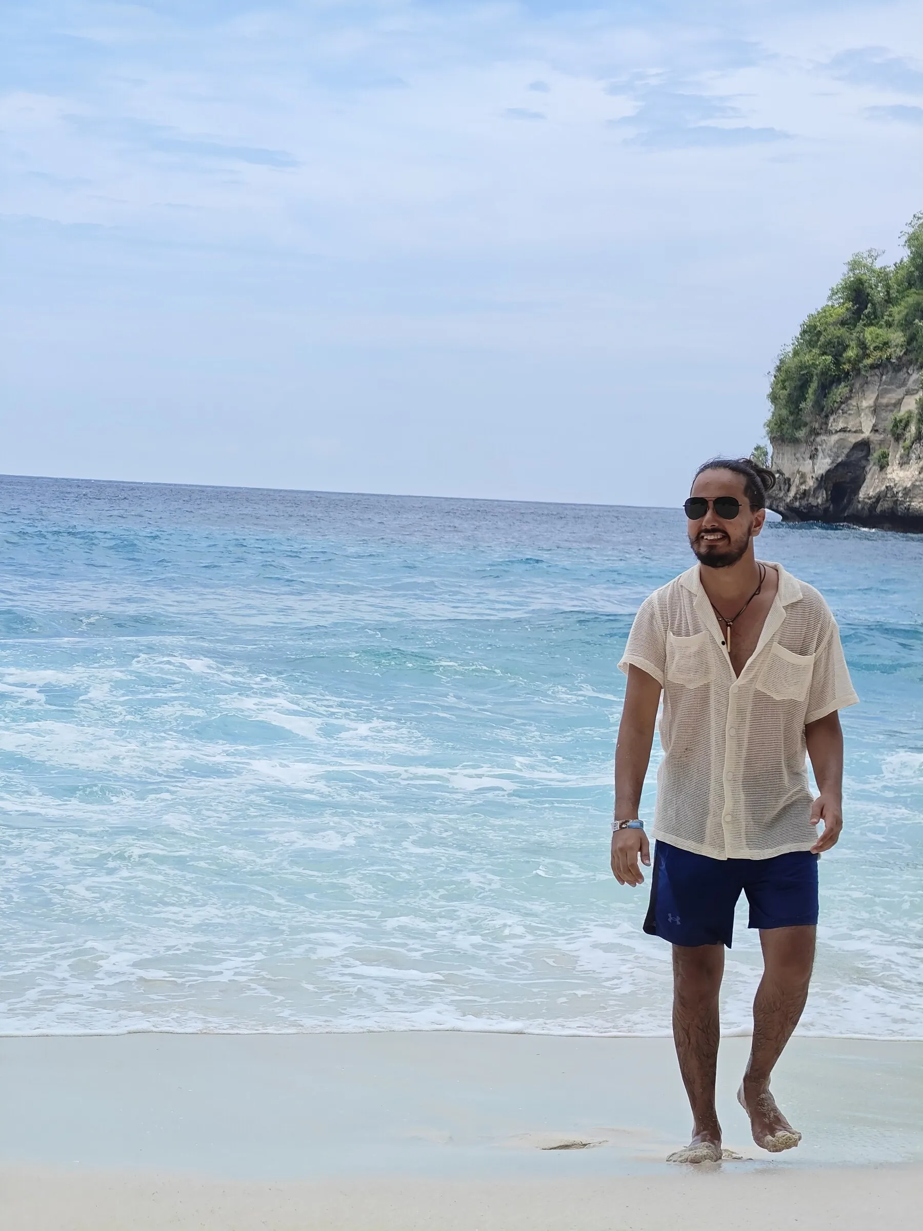 Lokesh walking along a bright blue shoreline in Bali.