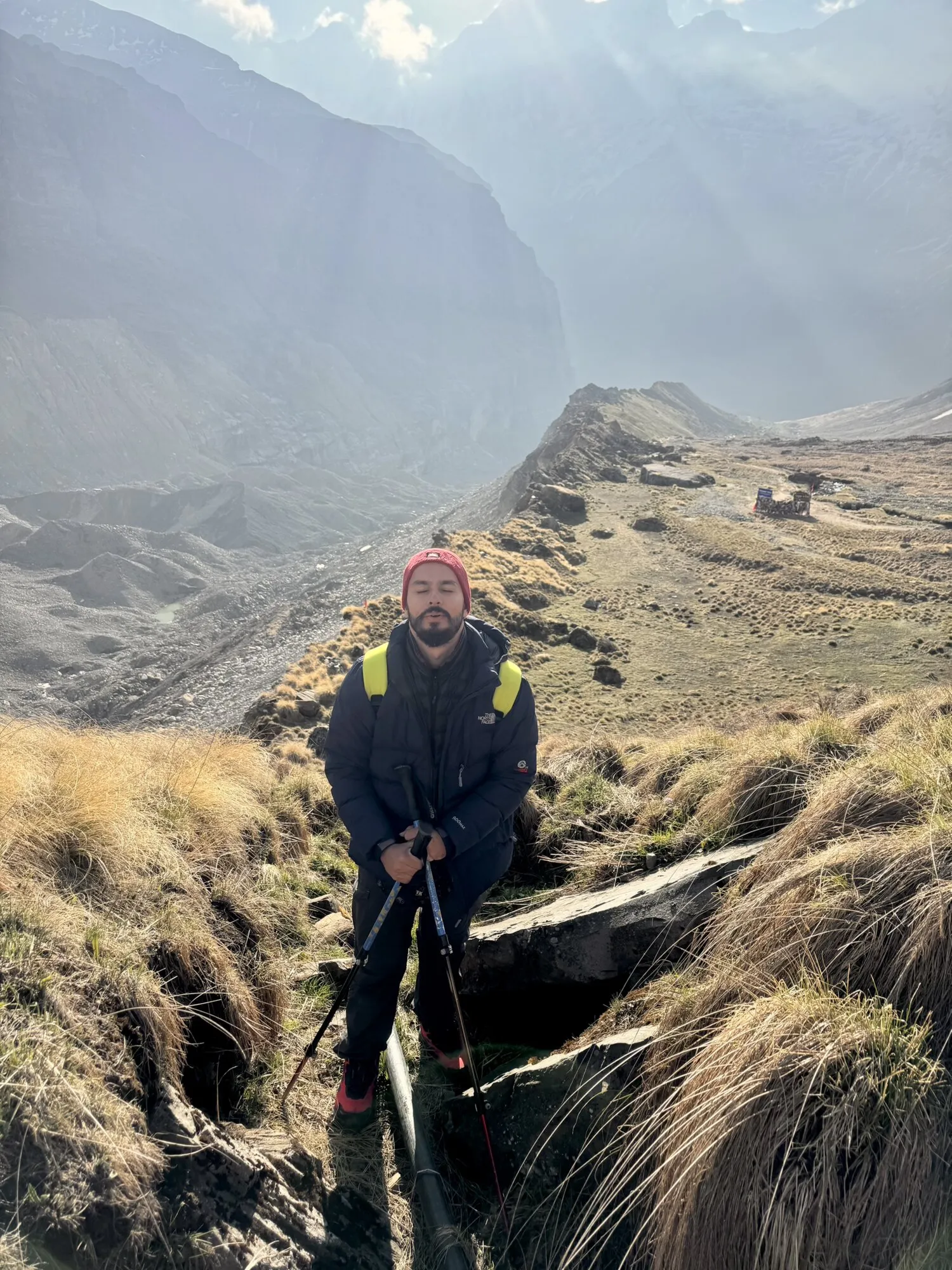 Lokesh pausing with trekking poles on a high mountain trail.