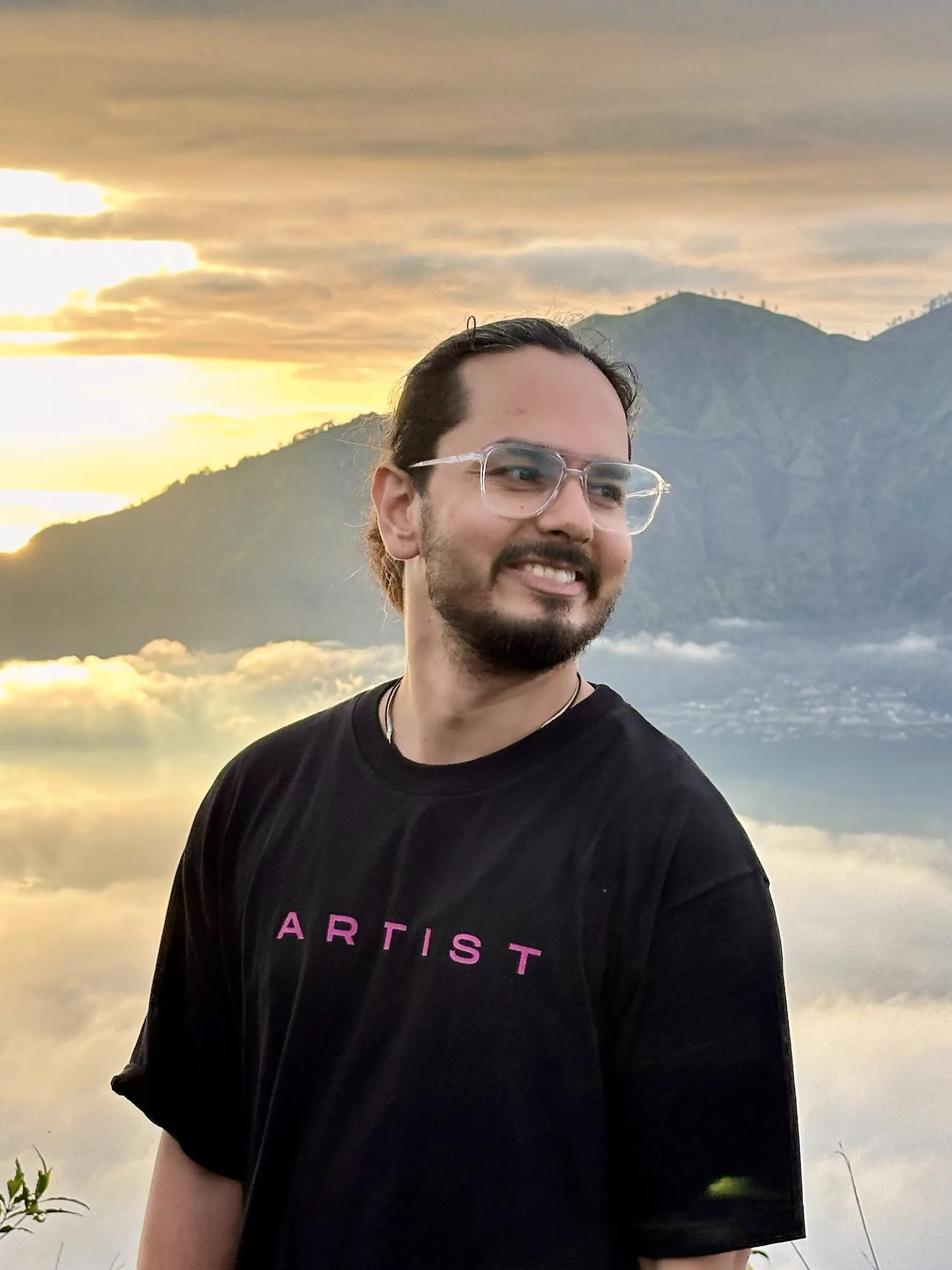 Lokesh wearing an Artist shirt at sunrise above a mountain cloudscape.