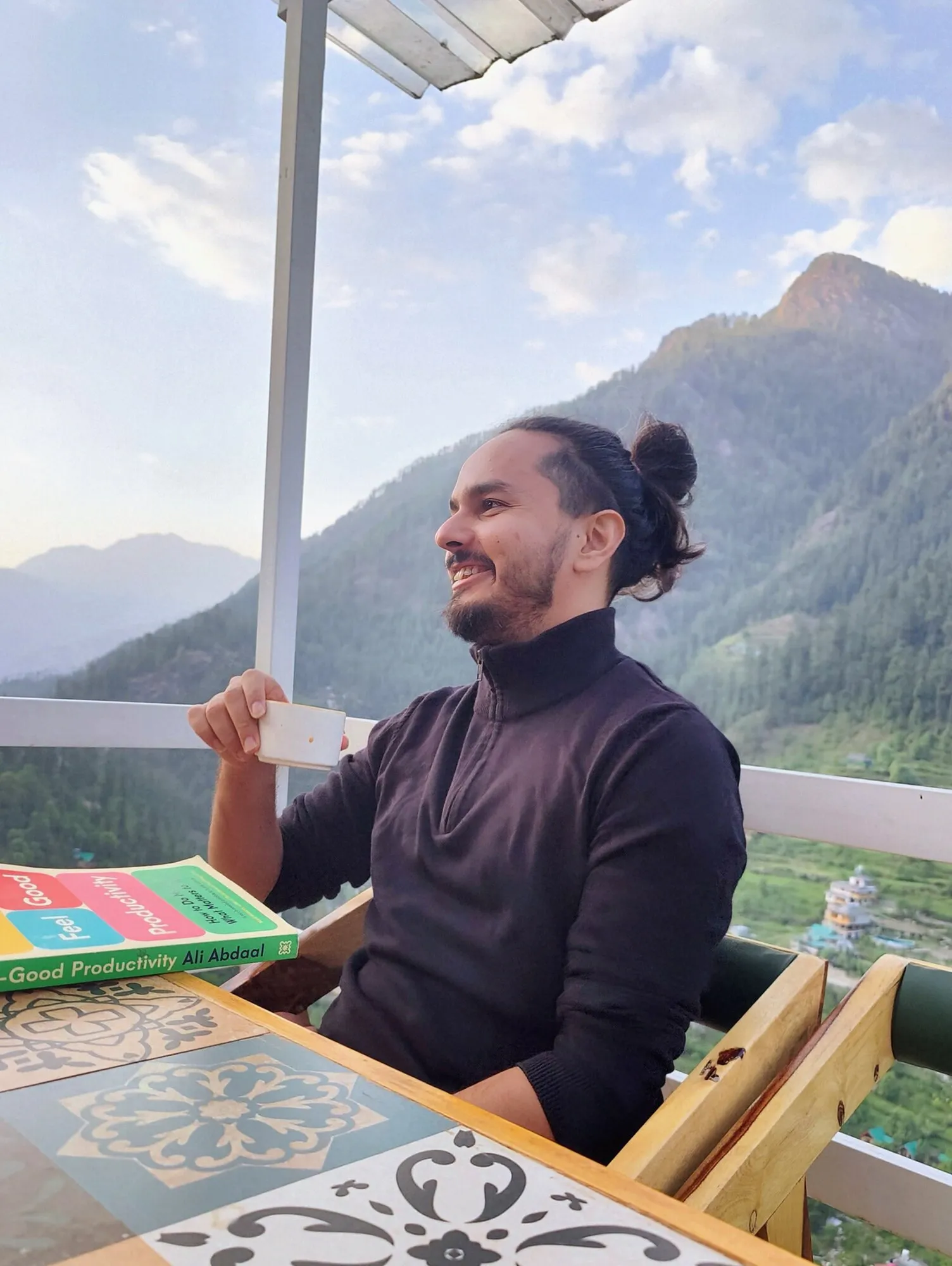 Lokesh taking a tea break overlooking a green mountain valley.