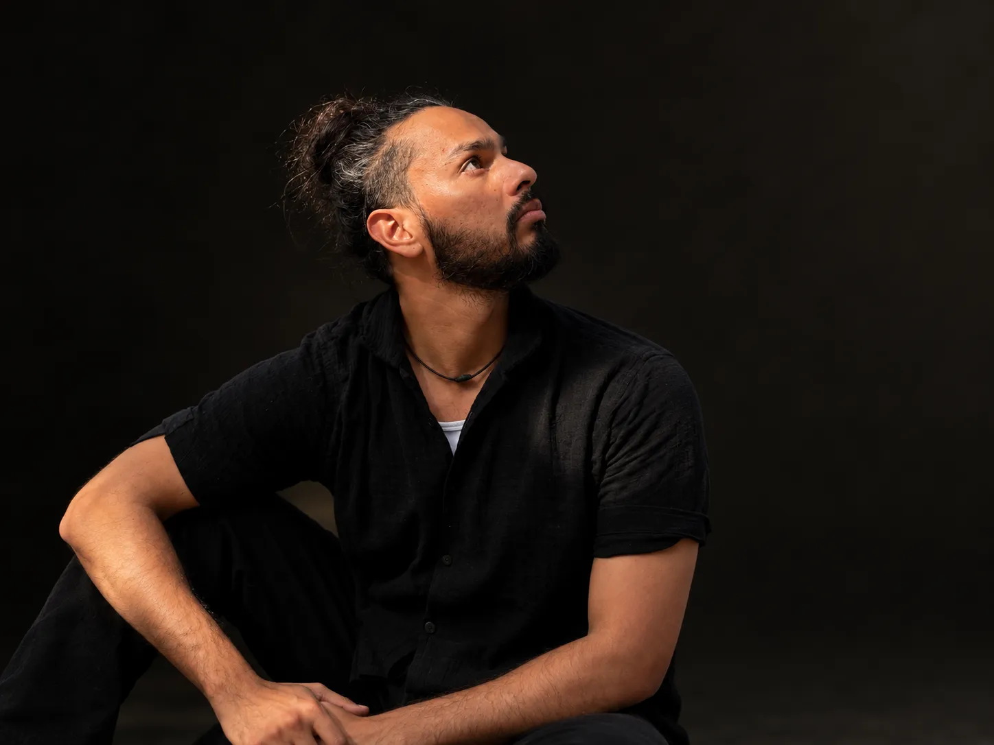Lokesh in dramatic side light, looking upward — contemplative portrait against a dark ground.